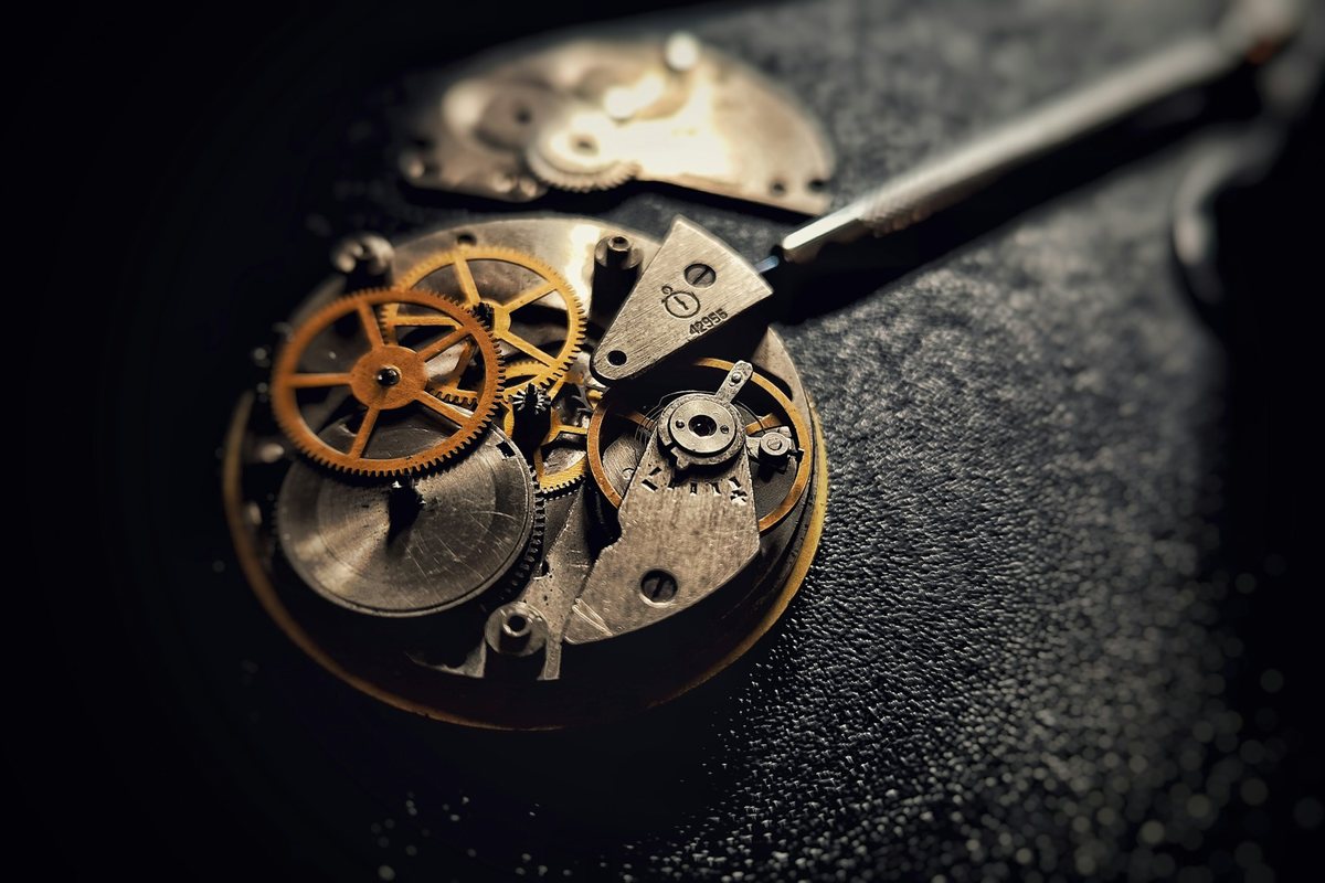 Mouvement de montre ouvert, rouages dorés et outil d'horloger, dans la pénombre
